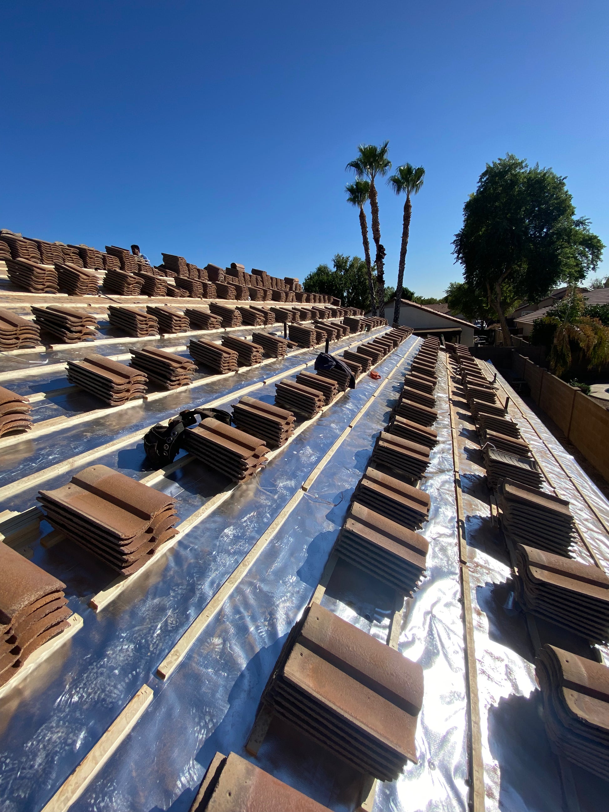 Stacks of curved tile roof shingles on RoofingFoil + Underlayment with palm trees in the background